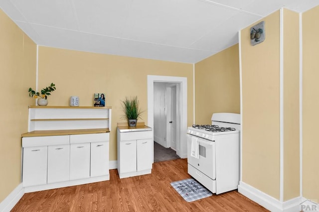710 Wilson Ave, Pueblo, CO 81004 - kitchen featuring white range with gas stovetop, light wood-style flooring, white cabinets, and baseboards