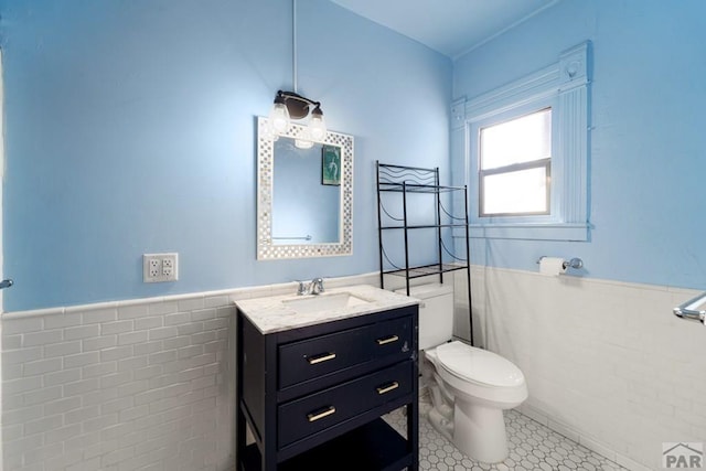 bathroom featuring a wainscoted wall, toilet, vanity, and tile walls