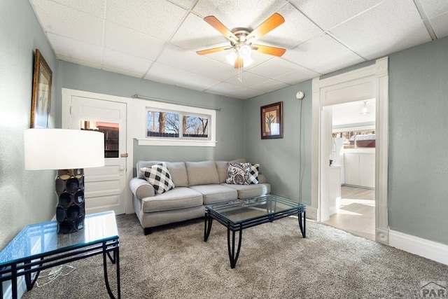 carpeted living area with a paneled ceiling, ceiling fan, and baseboards