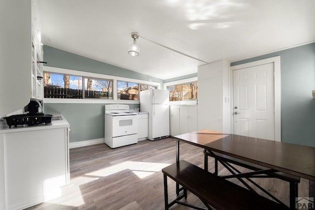 kitchen with white appliances, light wood-style flooring, vaulted ceiling, and white cabinets