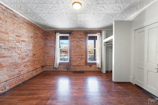 unfurnished bedroom featuring brick wall, an ornate ceiling, and dark wood-style flooring