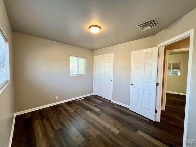 unfurnished bedroom featuring a closet, dark wood-style flooring, visible vents, and baseboards