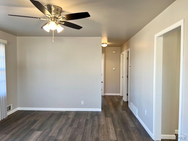 empty room featuring ceiling fan, visible vents, baseboards, and dark wood finished floors