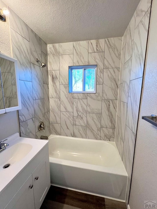 bathroom with a textured ceiling, a textured wall, wood finished floors, vanity, and shower / bathing tub combination