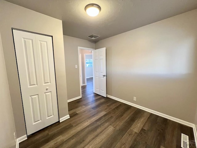 unfurnished bedroom featuring baseboards, a closet, visible vents, and dark wood-type flooring