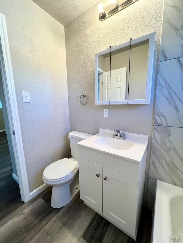 full bathroom with toilet, a textured wall, wood finished floors, and vanity