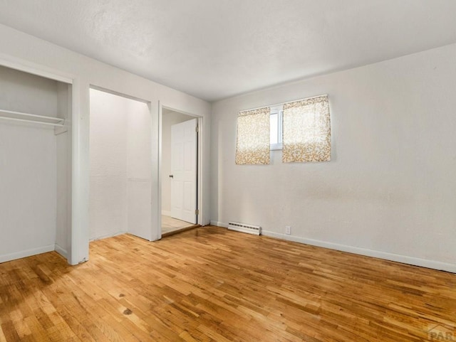 unfurnished bedroom featuring a baseboard heating unit, a closet, light wood-style flooring, and baseboards