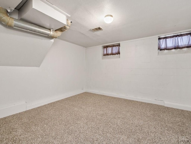 basement with a textured ceiling, carpet, visible vents, and concrete block wall