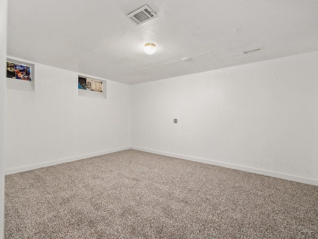 empty room with a textured ceiling, carpet flooring, visible vents, and baseboards