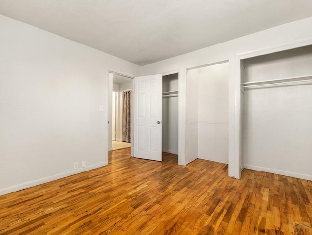 unfurnished bedroom featuring baseboards, wood finished floors, and multiple closets