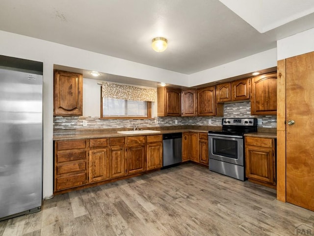 kitchen with wood finished floors, appliances with stainless steel finishes, brown cabinetry, and a sink