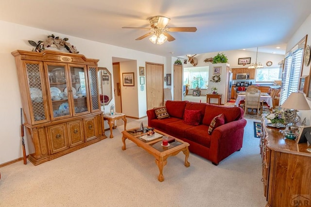 living area featuring baseboards, ceiling fan with notable chandelier, vaulted ceiling, and light colored carpet