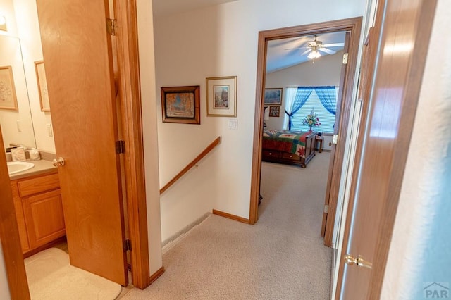 hall featuring light carpet, baseboards, vaulted ceiling, and an upstairs landing