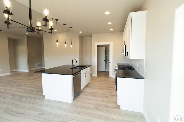 kitchen with dark countertops, white cabinetry, a center island with sink, and decorative light fixtures