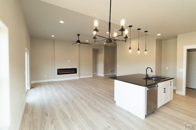 kitchen featuring dark countertops, hanging light fixtures, stainless steel dishwasher, a kitchen island with sink, and white cabinetry