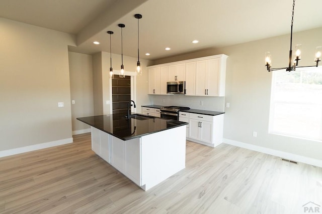 kitchen featuring hanging light fixtures, white cabinetry, stainless steel appliances, and an island with sink