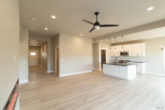 kitchen featuring white cabinets, dark countertops, an island with sink, stainless steel microwave, and decorative light fixtures