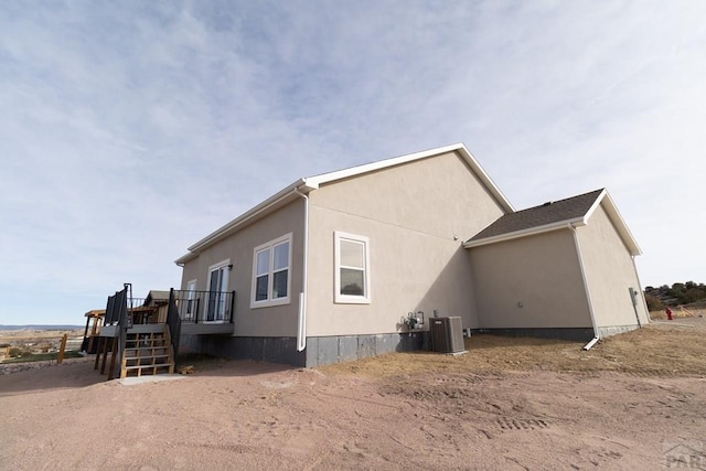 view of side of property featuring a wooden deck, stairs, central AC unit, and stucco siding