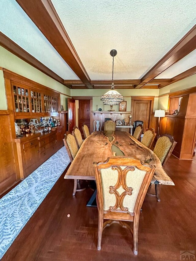 dining area with dark wood-type flooring, beamed ceiling, and a textured ceiling