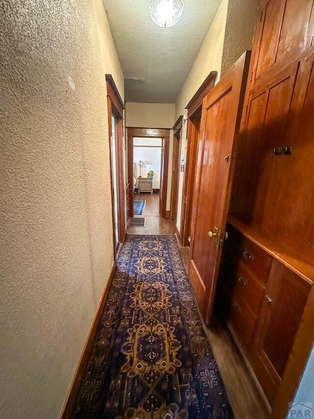 corridor with baseboards, a textured ceiling, and a textured wall