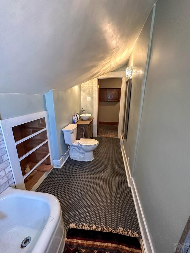 bathroom with lofted ceiling, baseboards, toilet, and a sink