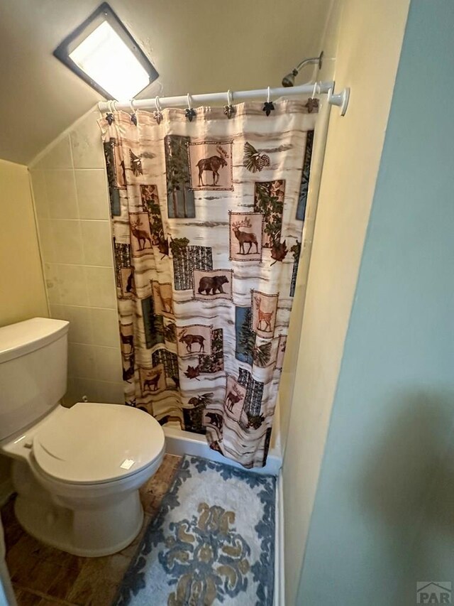 full bathroom featuring toilet, a shower with curtain, vaulted ceiling, and tile walls