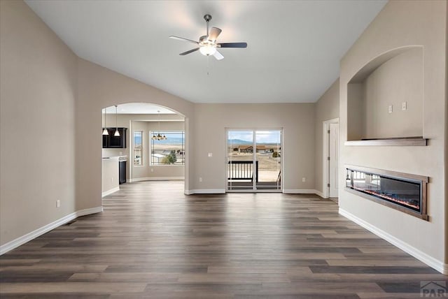 unfurnished living room featuring dark wood-type flooring, a glass covered fireplace, vaulted ceiling, and baseboards