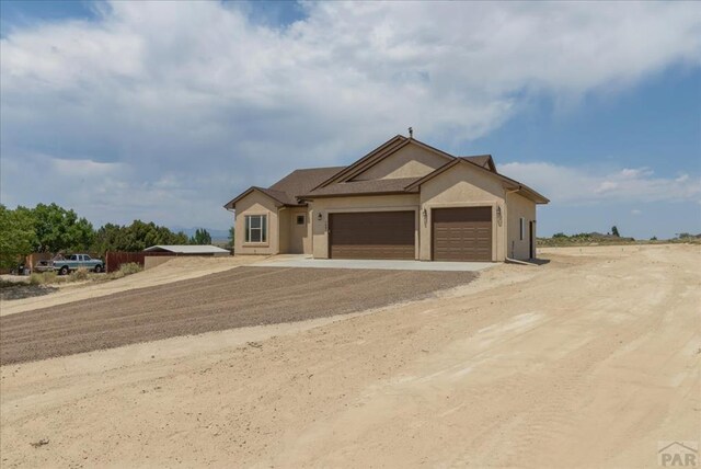 view of front of home featuring dirt driveway, an attached garage, and stucco siding