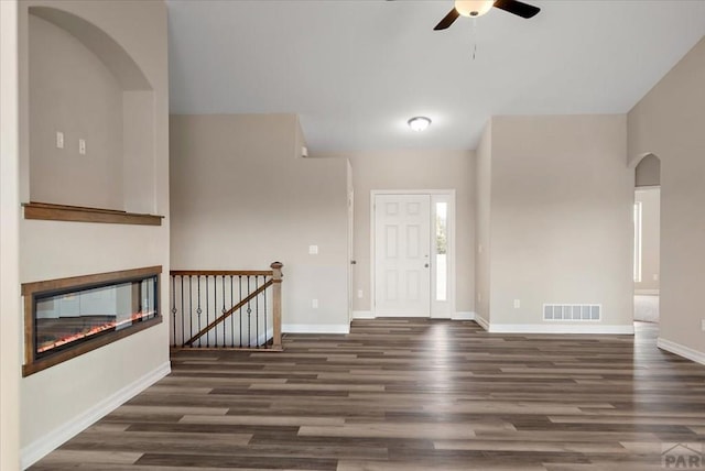 foyer entrance featuring arched walkways, wood finished floors, visible vents, baseboards, and a glass covered fireplace