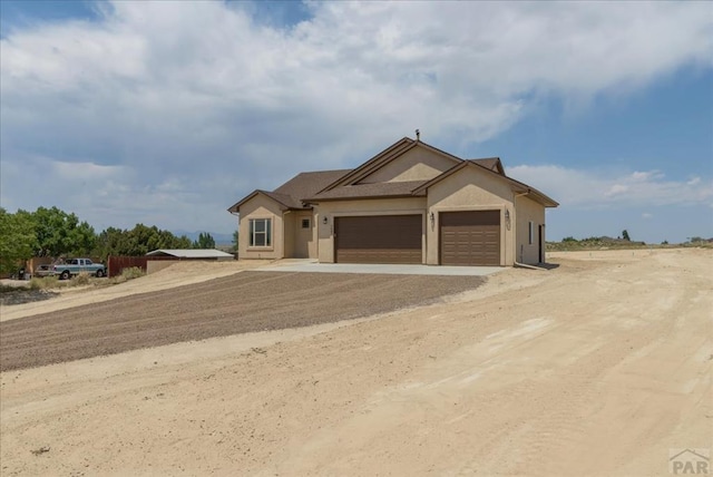 ranch-style home with a garage, dirt driveway, and stucco siding