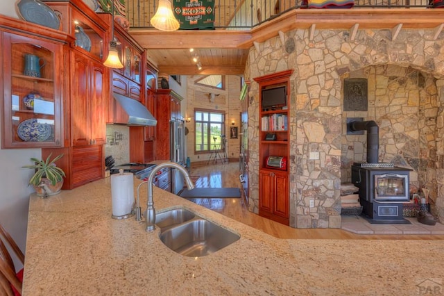 kitchen with light countertops, glass insert cabinets, a wood stove, a sink, and light wood-type flooring