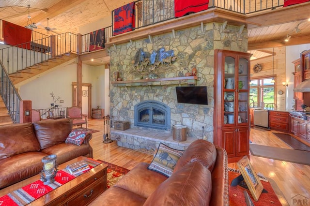 living room featuring wooden ceiling, light wood-style flooring, a fireplace, a towering ceiling, and beam ceiling