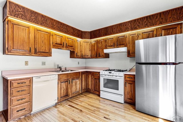 kitchen featuring white appliances, a sink, under cabinet range hood, brown cabinetry, and light countertops