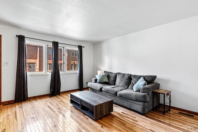 living area featuring light wood-type flooring, a textured ceiling, and baseboards