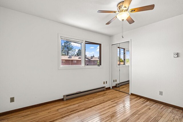 unfurnished room with a baseboard heating unit, plenty of natural light, light wood-style floors, and ceiling fan