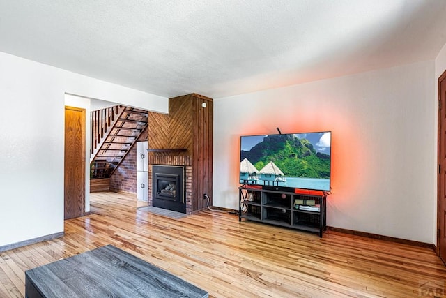 living room featuring stairs, wood finished floors, baseboards, and a brick fireplace