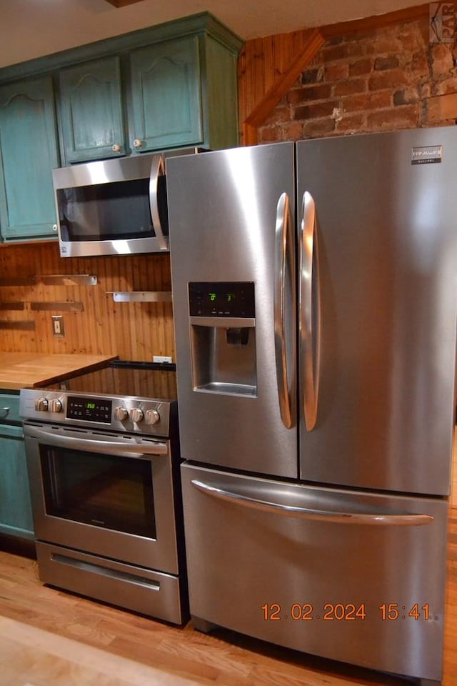 kitchen with light wood-type flooring, wooden walls, stainless steel appliances, and green cabinetry