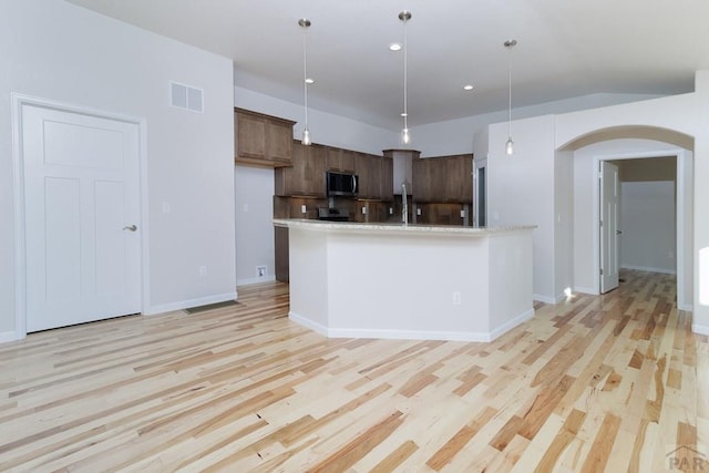 kitchen with arched walkways, light countertops, light wood-type flooring, stainless steel microwave, and pendant lighting