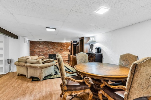 dining space with a drop ceiling, light wood-type flooring, and a brick fireplace