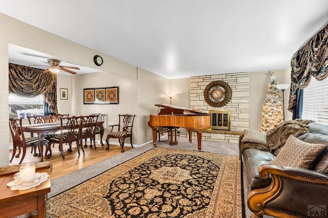 living area featuring wood finished floors, ceiling fan, a stone fireplace, and baseboards