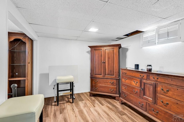 living area with a drop ceiling and light wood-type flooring