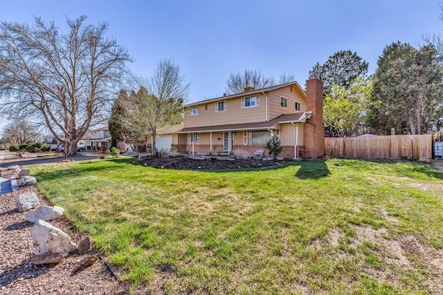 rear view of property featuring a yard, a chimney, covered porch, brick siding, and fence