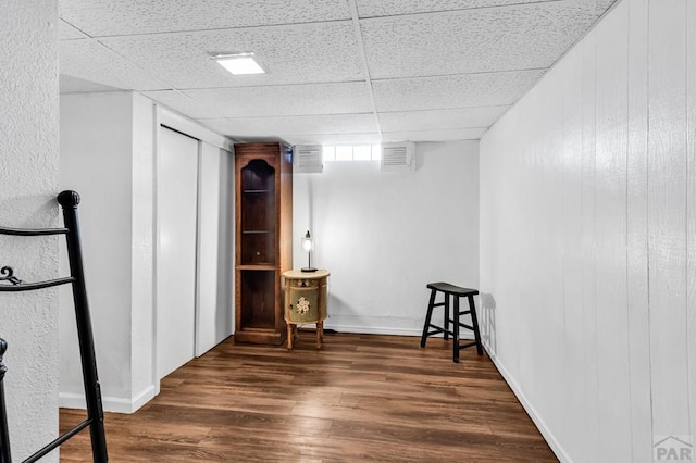 below grade area with visible vents, a drop ceiling, wood finished floors, and baseboards