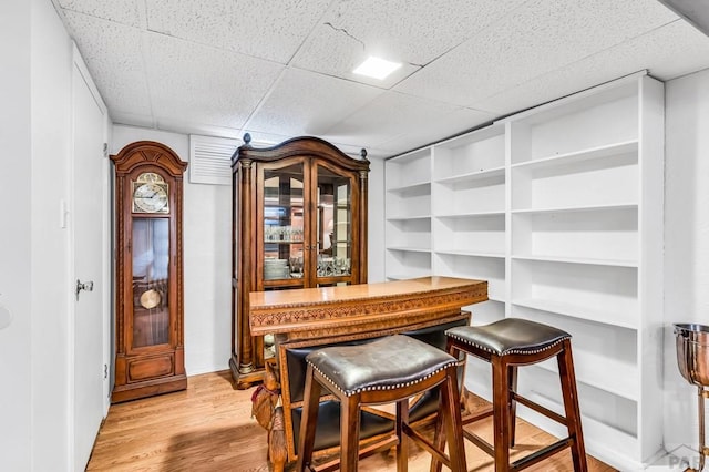bar with a drop ceiling, built in shelves, and light wood-style floors