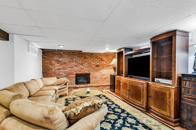 living room with a paneled ceiling, brick wall, and a fireplace