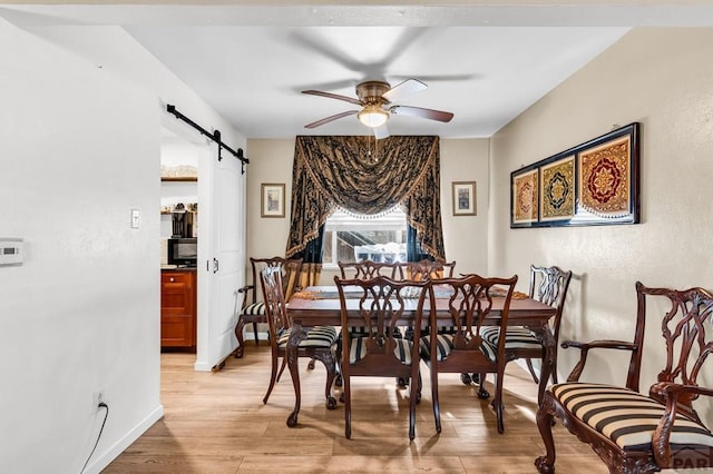 dining space with light wood finished floors, a ceiling fan, a barn door, and baseboards
