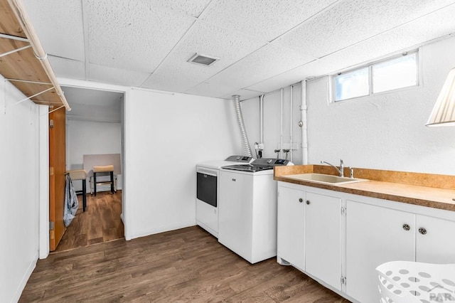 clothes washing area featuring a sink, washing machine and clothes dryer, cabinet space, dark wood-type flooring, and visible vents