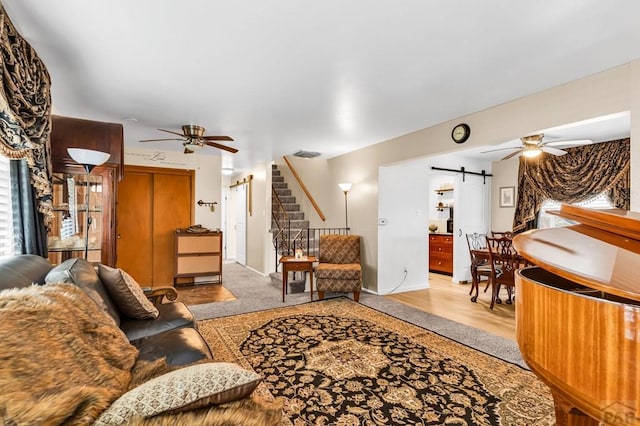 living area featuring stairway, a barn door, visible vents, baseboards, and a ceiling fan