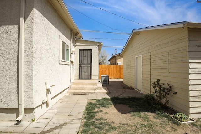 view of side of home featuring central AC unit, fence, and stucco siding