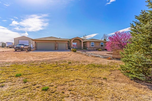 ranch-style house with stucco siding, an attached garage, stone siding, and a front yard